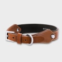 A dog collar in smooth, natural bovine leather, handmade in a Polish artisan workshop. Designed by the Italian designer Francesco Rigucci, it is recognisable by its signature shape and the jewellery-like metal studs carrying the brand logo. The outer layer is caramel vegetable-tanned bovine leather with contrasting beige stitching, over soft padding and a chocolate leather lining. The D-ring, buckle and logo studs are solid brass in silver finish, nickel-free and protected with a durable polished coating. Adjustable length – check the measurements to choose the right size for your dog. Available on its own or as a set with the matching leather leash and lambskin gloves.