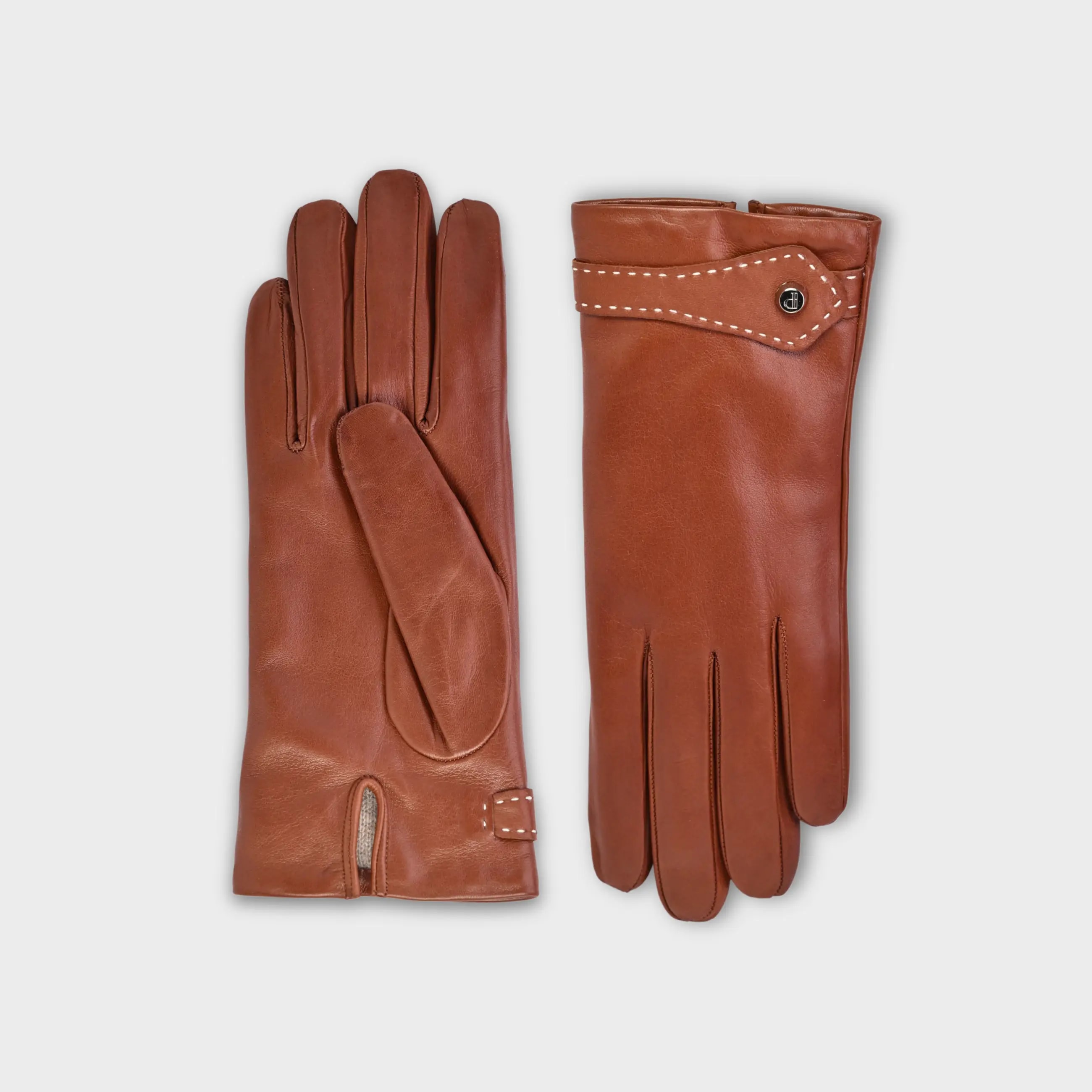 Handcrafted from smooth caramel lambskin and lined with natural beige cashmere. Finished with a decorative, hand-stitched leather strap in contrasting beige thread. Featuring the signature brass logo closure in silver, nickel-free and protected with a durable, polished finish. Made in an artisanal workshop in Italy. Available in sizes 7, 7.5, 8, 8.5, 9, 9.5 (Italian sizing).