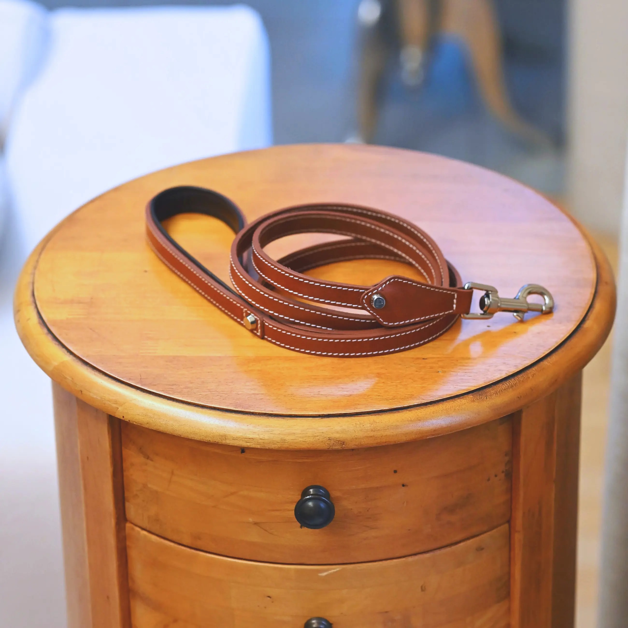 A dog leash in smooth, natural bovine leather, handmade in a Polish artisan workshop. Designed by the Italian designer Francesco Rigucci, it is recognisable by its signature shape and the jewellery-like metal studs carrying the brand logo. Made from caramel vegetable-tanned bovine leather with contrasting beige stitching. The handle is finished with a chocolate leather lining. The snap hook and logo studs are solid brass in silver finish, nickel-free and protected with a durable polished coating. Fixed length of 175 cm. Available in two widths: 1.5 cm and 2.2 cm. Available on its own or as a set with the matching leather collar and lambskin gloves.