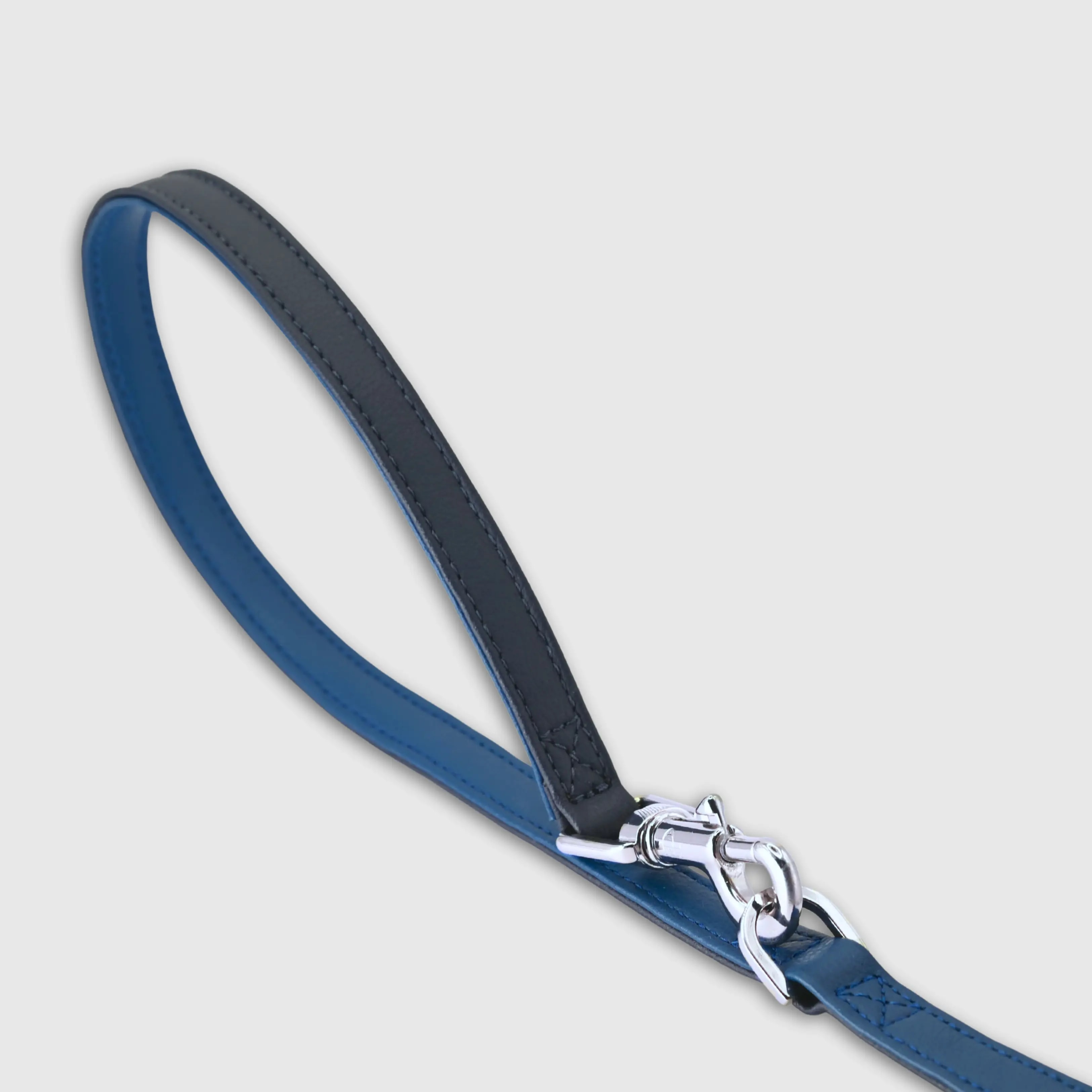 A dog leash in vegan cactus leather, handmade in a Polish artisan workshop. Designed by the Italian designer Francesco Rigucci, it is recognisable by its signature shape and the jewellery-like metal studs carrying the brand logo. Made from two shades of cactus leather – navy and cobalt – with matching navy stitching. The snap hook and logo studs are solid brass in silver finish, nickel-free and protected with a durable polished coating. Two snap hooks let you clip the leash in several different ways. Adjustable length: 230 cm, 150 cm and 115 cm. Choose between two widths: 1.5 cm and 2.2 cm. Available on its own or as a set with the matching cactus leather collar.